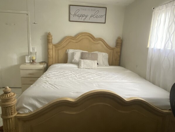 A neatly made bed with a wooden headboard, a bedside table with a lamp, and a framed sign on the wall.