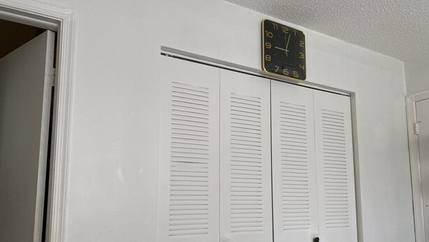 A white closet with louvered doors and a wall-mounted clock. - Beautiful 2 bedroom house walking distance from hard rock stadium (Miami Gardens)