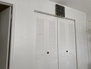 A white closet with louvered doors and a wall-mounted clock.