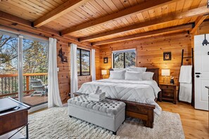 Un dormitorio de cabaña de madera con una cama grande, un banco, un escritorio y un balcón con sillas.