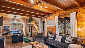 A cozy wooden cabin interior with a pool table, a sofa, and a fan. - Spacious, Modern Mountain Cabin with Hot Tub (Running Springs)