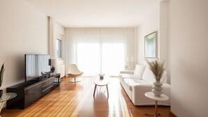 Uma sala de estar moderna com uma televisão de tela plana, um sofá, uma mesa de centro e uma mesinha lateral com um vaso.