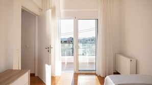 Quarto com piso de madeira, uma cama, radiador e porta de vidro deslizante para uma varanda.