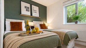A hotel room with two beds, a breakfast tray with fruits and drinks, and framed wall art.