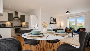 A modern kitchen with white cabinets, a built-in oven, and a dining area with a round table and chairs.