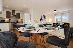 A modern kitchen with white cabinets, a built-in oven, and a dining area with a round table and chairs.
