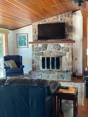 A living room with a stone fireplace, a mounted TV, a blue armchair, and a leather couch.