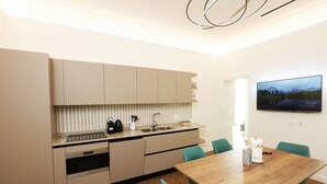 A modern kitchen with a wooden dining table and teal chairs, a built-in oven, and a large flat-screen TV on the wall. - Appartamento nel Centro Storico di Sorrento, Nuovo, con Vista (Sorrento)