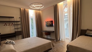 A hotel room with two beds, a desk, a chair, a coat rack, and a painting on the wall. - Appartamento nel Centro Storico di Sorrento, Nuovo, con Vista (Sorrento)
