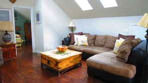 A living room with a brown leather sofa, a wooden coffee table, and a wooden chest. There is a lamp on a side table and a wall-mounted lamp.