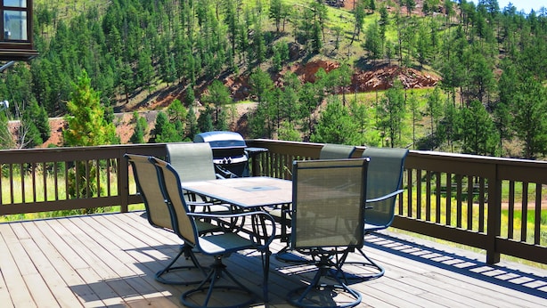 A deck with outdoor furniture and a grill, overlooking a forested hillside.
