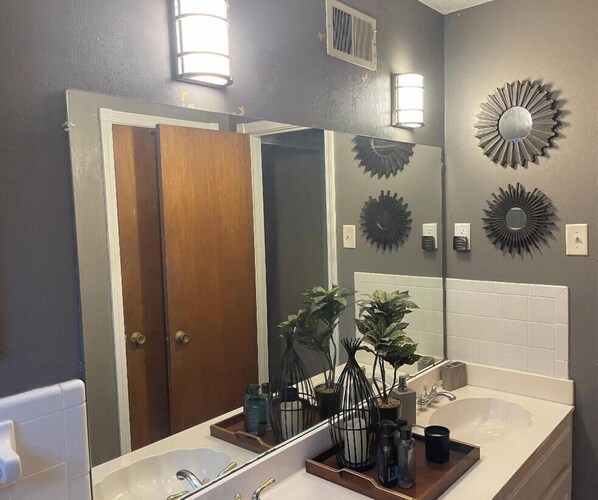 A bathroom with a large mirror, two sinks, decorative wall sconces, and potted plants. - Eclectic 4 Bedroom Getaway with Private Pool! (Memphis)