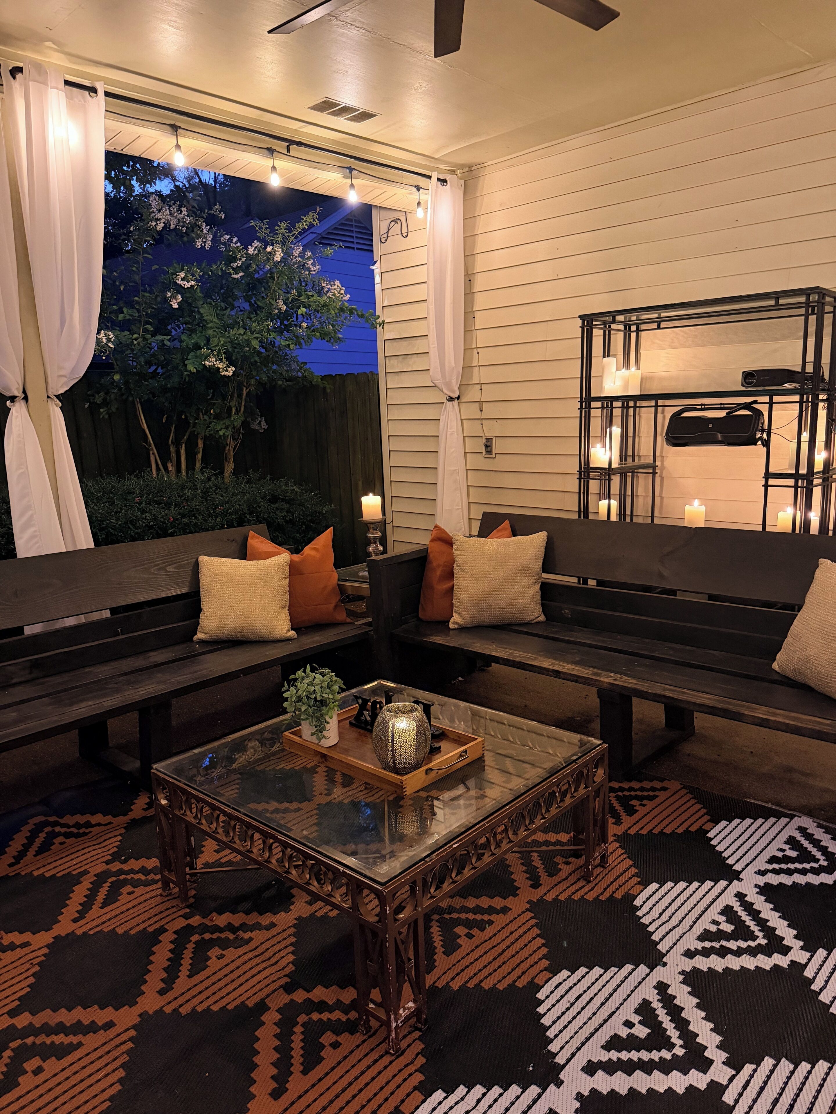 An outdoor seating area with a glass-top coffee table, cushioned benches, and a patterned rug.