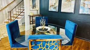 A modern dining area with a glass table surrounded by blue upholstered chairs, a decorative centerpiece, and framed artwork on the wall. - Eclectic 4 Bedroom Getaway with Private Pool! (Memphis)