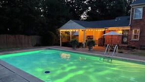 A swimming pool with a wooden deck and a covered patio area with string lights. - Eclectic 4 Bedroom Getaway with Private Pool! (Memphis)