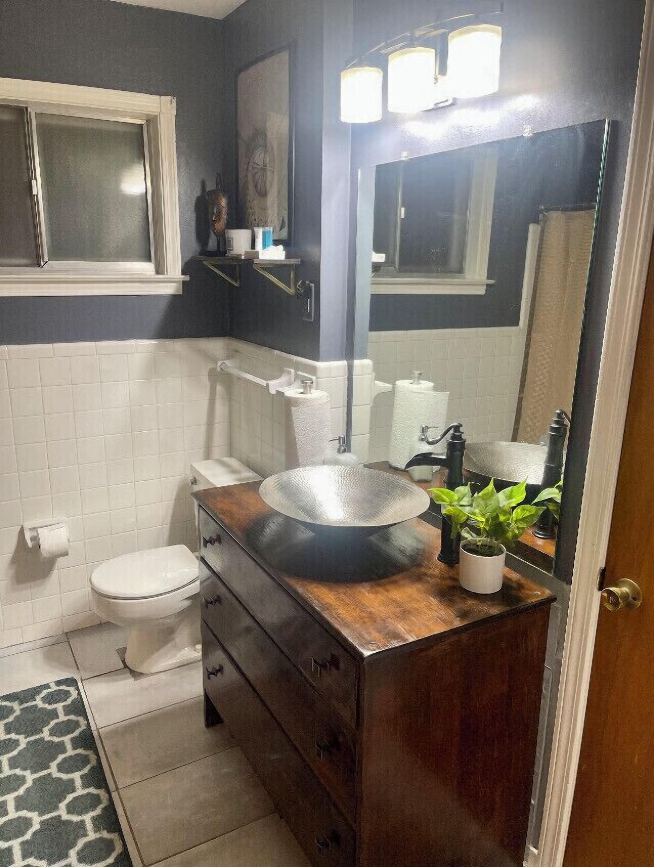 Ein Badezimmer mit Holzwaschtisch, einem runden Waschbecken, einem Spiegel und einer Toilette.