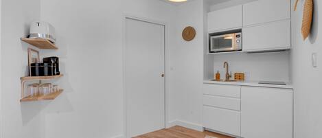Een moderne keuken met witte kasten, een magnetron en een hangende lamp.