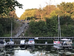 Eine Anlegestelle mit Booten, eine Treppe, die zu einer Plattform führt, und ein bewaldeter Hügel im Hintergrund.