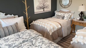 Et soveværelse med seng, natbord, lampe, knagerække og et spejl på væggen.