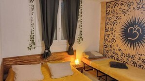 A room with a bed, a bench, and a wall with a sun-like design.