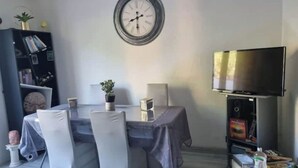 Ein Essbereich mit Tisch, Stühlen, einer Uhr, einem Bücherregal und einem Fernseher.