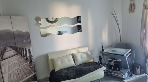 A bedroom with a bed, a side table, a mirror, and a wall-mounted shelf.