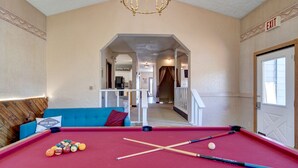 A pool table with balls, a blue sofa with a pillow, and an exit sign. - Suite102 "The Imperial Eagle" (Custer)