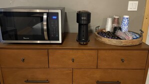 A microwave, espresso machine, and a basket with cups and containers on a wooden cabinet. - Suite102 "The Imperial Eagle" (Custer)