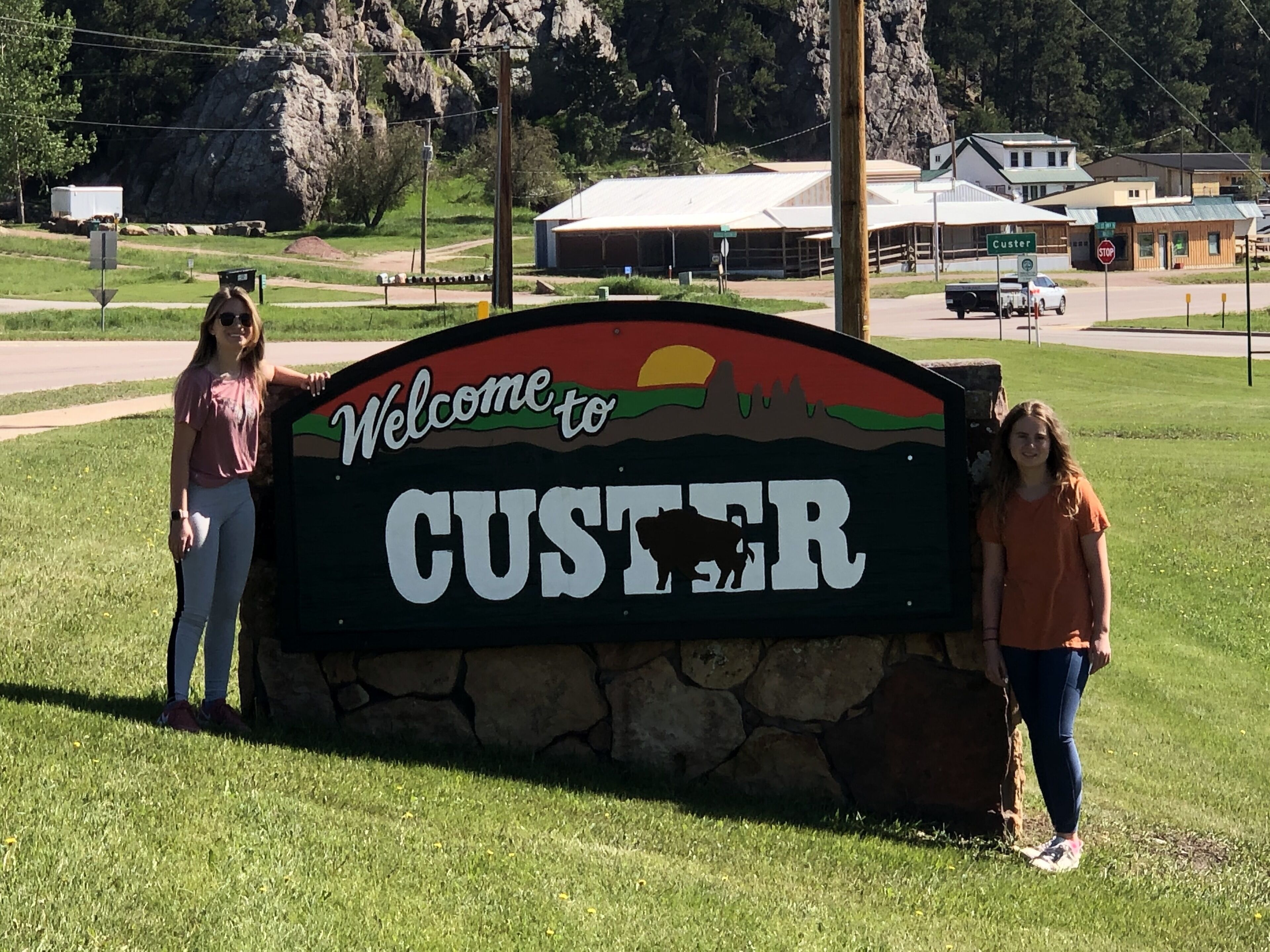 A welcome sign for Custer with a silhouette of a bison, a sunset, and a mountain range.
