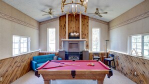 A pool table in a room with wooden walls, a fireplace, and a ceiling fan. - Suite102 "The Imperial Eagle" (Custer)