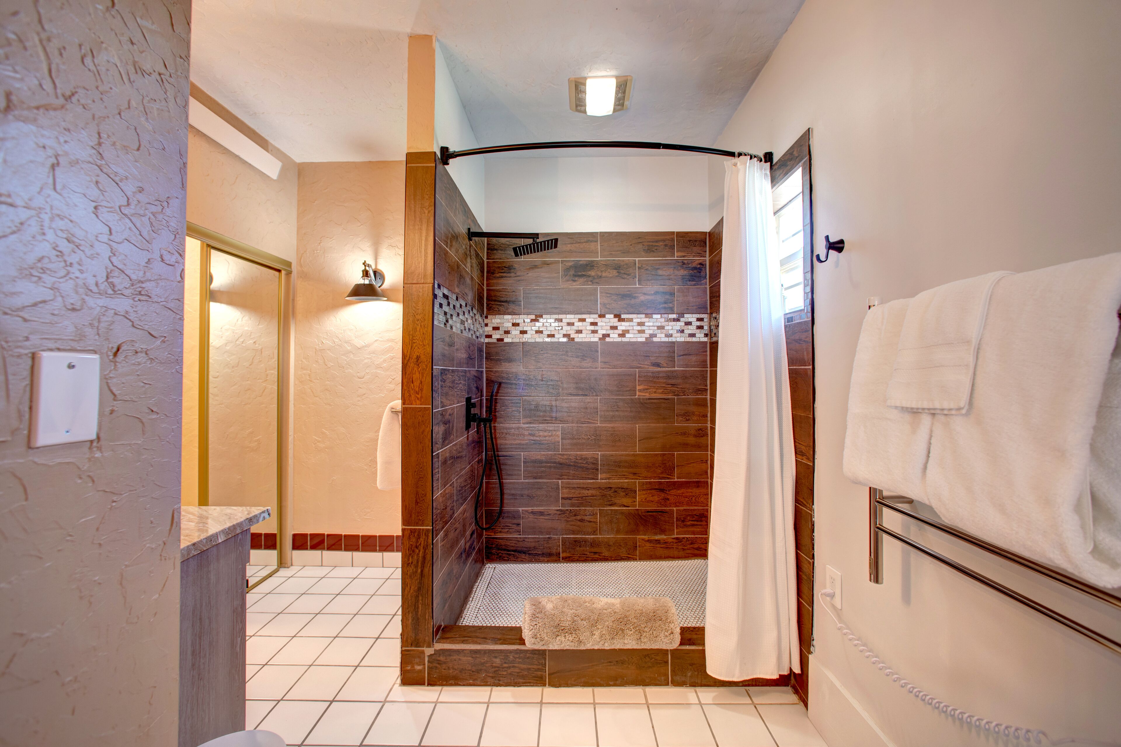 A modern bathroom with a shower, tiled walls, a towel rack, and a visible phone.