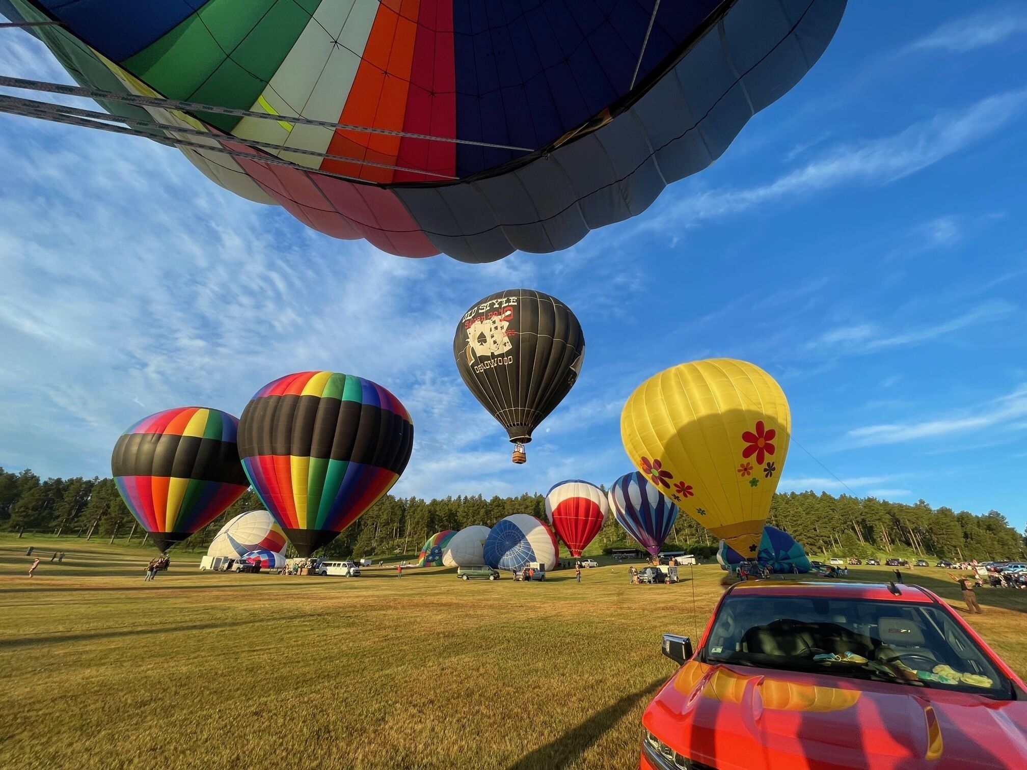 A field of colorful hot air balloons with a red car in the foreground.