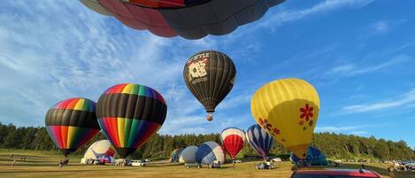 Un campo lleno de coloridas globos aerostáticos, con un auto rojo en primer plano.