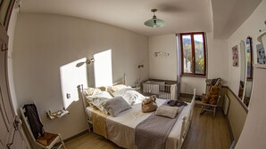 A bedroom with a bed, a chair, a crib, and a window.