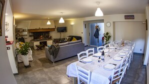 A dining area with a long table set for six, a grey sofa, and a kitchen in the background.