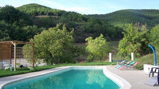 A swimming pool with lounge chairs and a pergola, surrounded by lush greenery and hills.