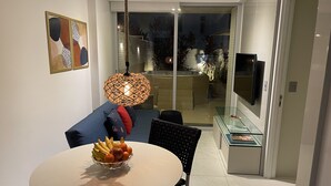 Uma sala de estar moderna com uma mesa de jantar, cadeiras, televisão e uma varanda com porta de vidro.