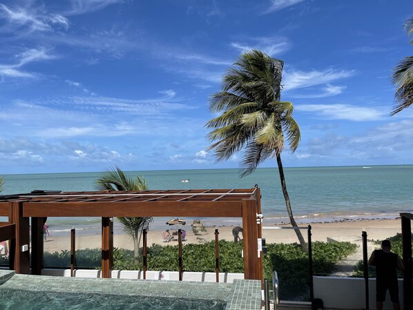 A beach view from a balcony with a wooden pergola, a pool, and a view of the ocean and beach. - Pé na areia do Caribessa - Branco Haus (João Pessoa)