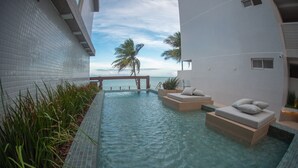 Área da piscina com vista para o oceano, uma espreguiçadeira e um pequeno espaço para sentar.