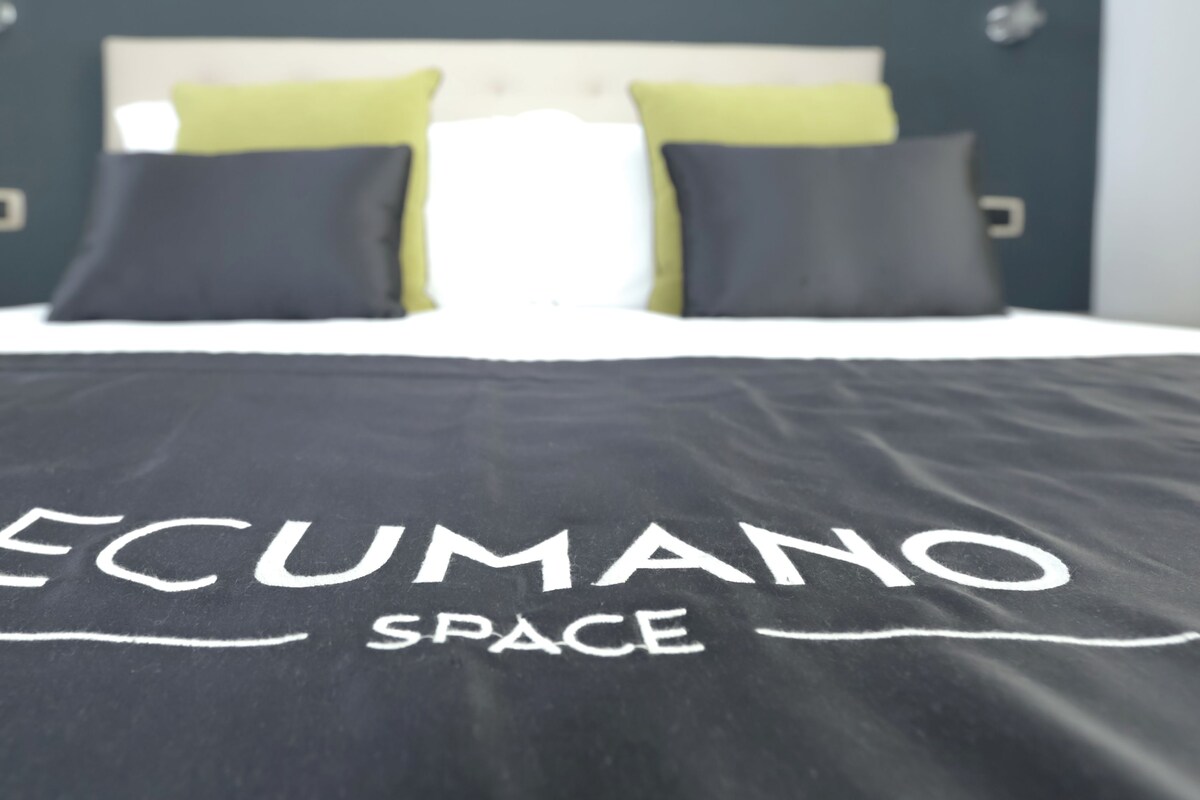 A bed with a black bedspread that reads "ECUMANO SPACE".