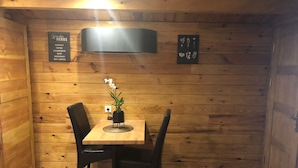 Ein Holzinnenraum mit Tisch und Stühlen, einem Schild mit der Aufzählung von Küchenkräutern sowie einer Wandleuchte.