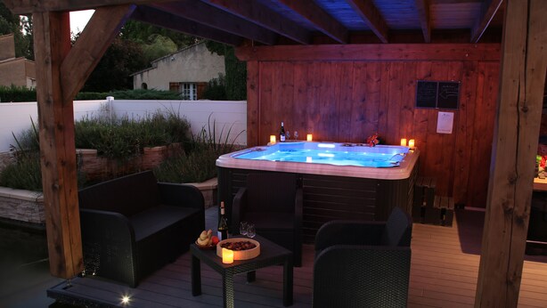 Eine Holzterrasse mit Whirlpool, Sitzgelegenheit und einem Tisch mit Kerzen und Flaschen.