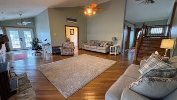A spacious living room with hardwood floors, a large rug, a grey sofa, and a ceiling fan.