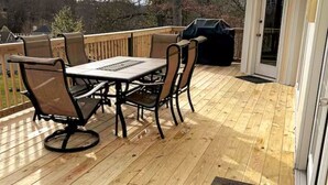 Una terraza de madera con mesa, sillas, una parrilla y una puerta.