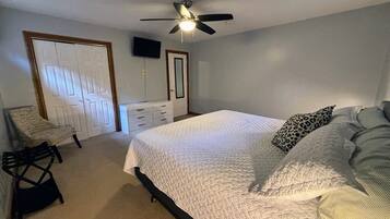 A bedroom with a bed, a ceiling fan, a TV on the wall, and a door.