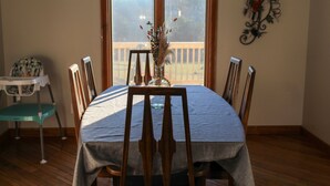 Una mesa de comedor con mantel azul, rodeada de sillas de madera y un jarrón con flores secas en el centro.