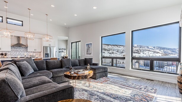 A spacious living room with a gray sectional sofa, a wooden coffee table, and a large window offering a view of a snowy landscape.