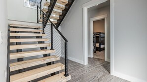 A staircase with wooden steps and a black metal railing, leading to a room with a grey floor and a white door.