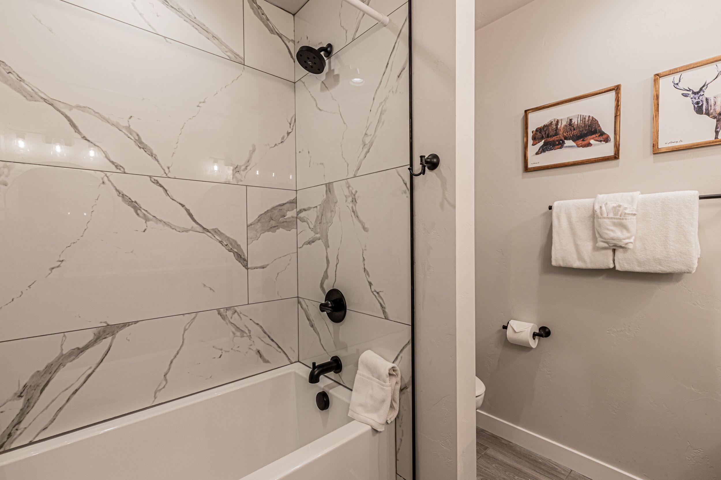 A bathroom with marble tiles, a bathtub, a shower, and two framed pictures on the wall.