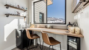 A kitchen with a large window, wooden shelves with glasses, a coffee machine, and a dishwasher.